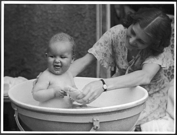 Baby Bath 1930S. A doting young mother gives her baby a bath in a tub, much to its delight