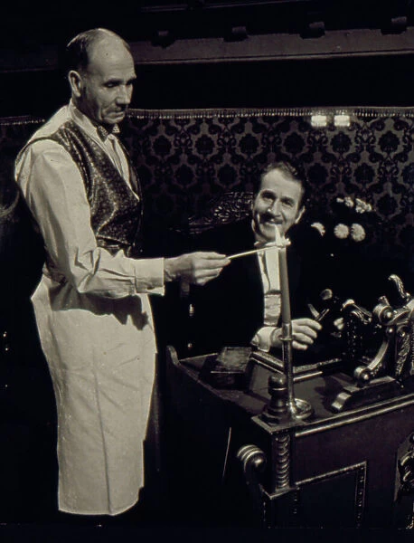 Two of the cast of the Old Time Music Hall TV show, known as The Good Old Days, filmed at the City Varieties in Leeds. The man on the left lights a candle, while the compere, played by the actor Leonard Sachs, smiles benignly. Date: 1960s