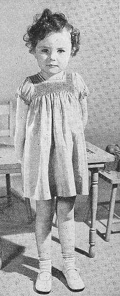 A child model wearing a smocked dress. Date: 1935