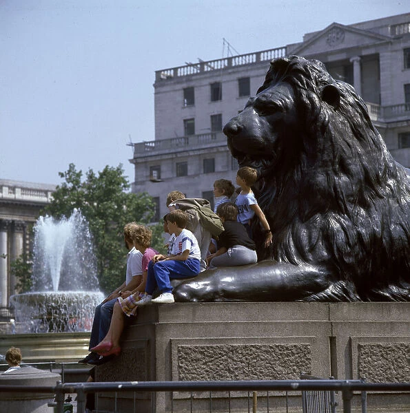 Children and adults sit on a Landseer Lion, Trafalgar Square