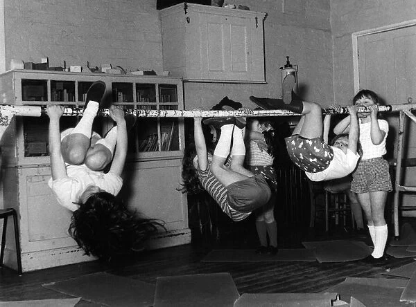 Children hanging from a pole, doing excercises during a gym class. Date: 1960s