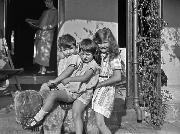 Three children sitting on a toy bear in a garden