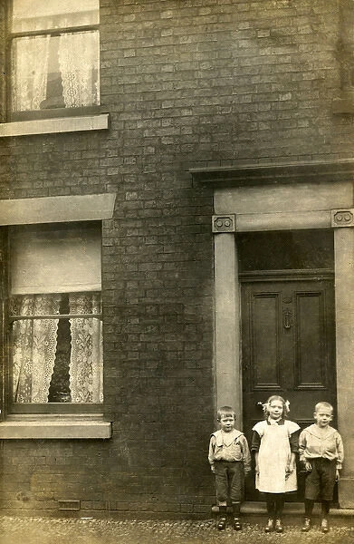 Three children stand outside their front door