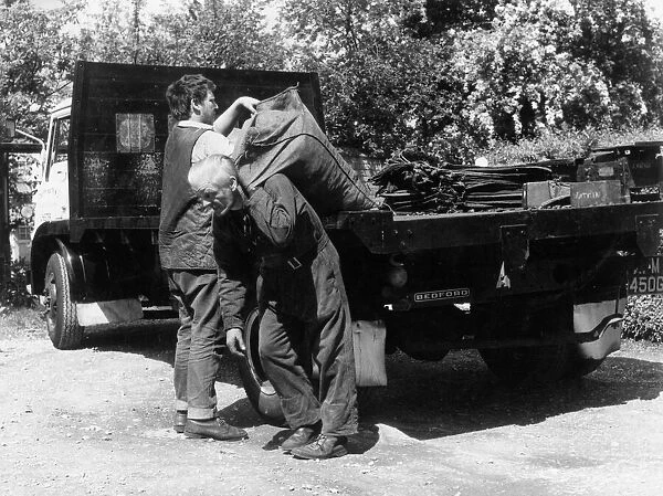 Coal Men 1960S. Two coal men, young and old, lift heavy sacks of coal off their lorry