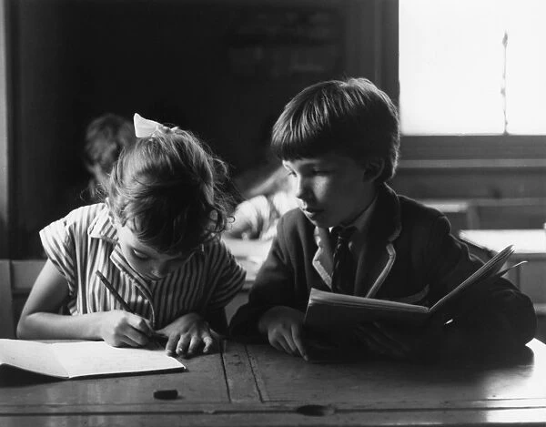 Copying Schoolboy. A schoolboy tries to copy his neighbours work. Date: late 1960s