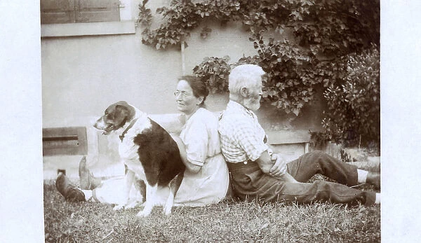 Couple sitting back to back in a garden, with dog