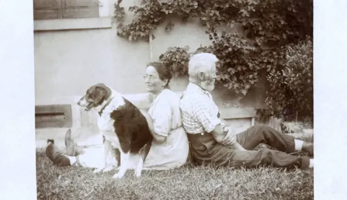Framed Print : Couple sitting back to back in a garden, with dog