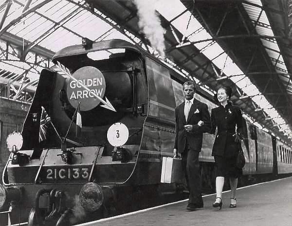 A couple walk arm in arm on a railway platform, beside the luxury locomotive the Golden Arrow, which linked London to Dover, where passengers caught the ferry to Calais, France. Date: 1947