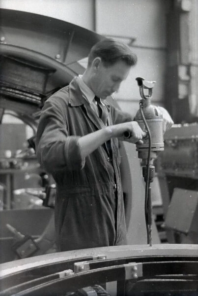 An engineer in overalls working with a large hand drill