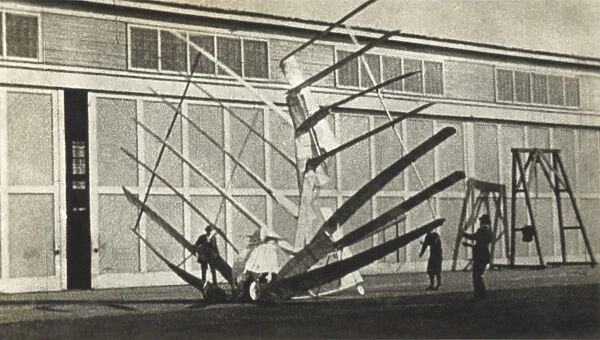 Gerhardt Cycleplane. Men Inspecting Crashed Gerhardt Cycleplane with Hangars Behind Date