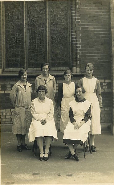 Group of six women, wearing aprons or overalls. They look as if they are staff at a