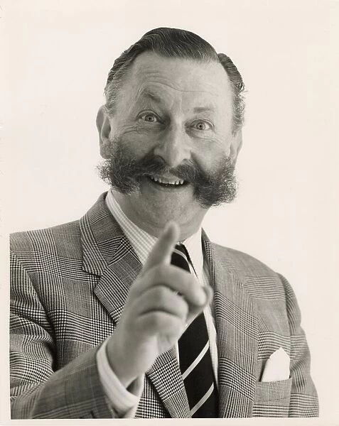 Head and shoulders portrait of a smartly dressed man with a bushy moustache pointing