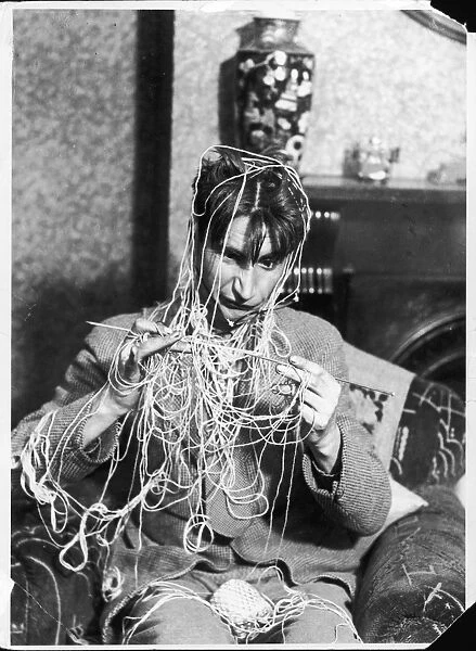 Knitting Expert. A young man in an armchair gets himself in rather a tangle