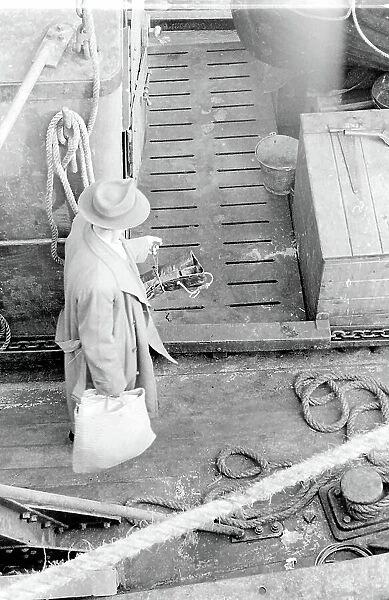 Life on a North Sea trawler - aerial view onto the deck - man in raincoat and trilby hat, carrying a shopping bag. Date: 1960s
