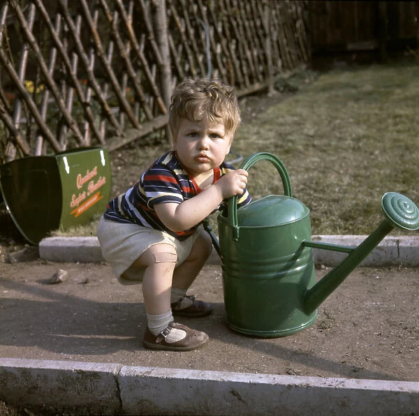 Little boy with green watering can in a garden