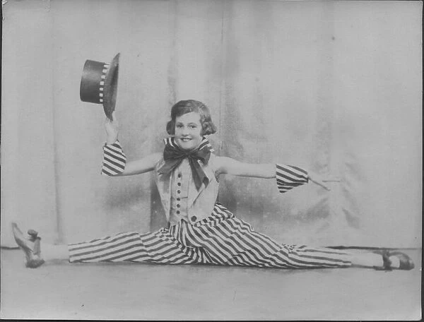 A little girl does the splits in a jolly stage costume of striped trousers and top hat