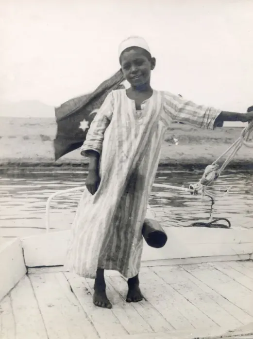 Framed Print : The little son of a ferryman at Luxor, Egypt, steers his fathers boat with his leg Framed Print : The little son of a ferryman at Luxor, Egypt, steers his fathers boat with his leg