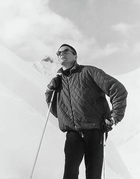 A male skier wearing a quilted jacket poses on the slopes. Date: late 1960s