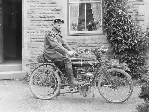 Man on an early motorcycle in front of a house
