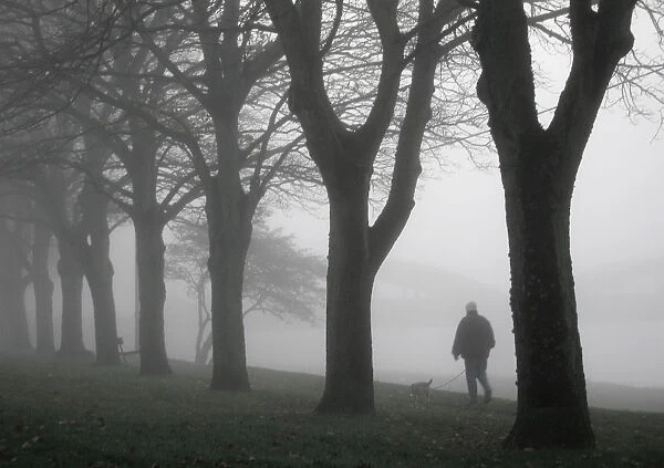 Man walks his dog in thick fog along banks of the River Dee