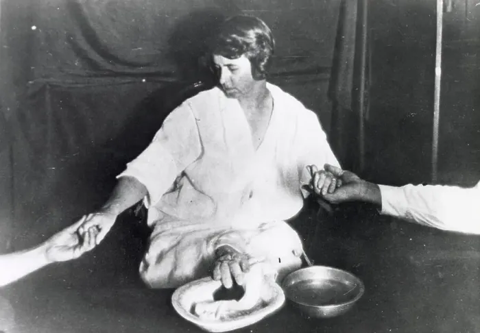 Framed Print : Margery, in trance and her wrists held by sitters, exudes ectoplasm forming a teleplasmic hand from somewhere between her legs Date: circa 1924 Framed Print : Margery, in trance and her wrists held by sitters, exudes ectoplasm forming a teleplasmic hand from somewhere between her legs Date: circa 1924