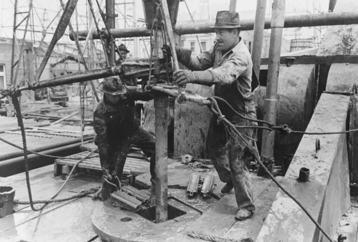 Framed Print : Oil field workers adding a length of pipe to drill stream by