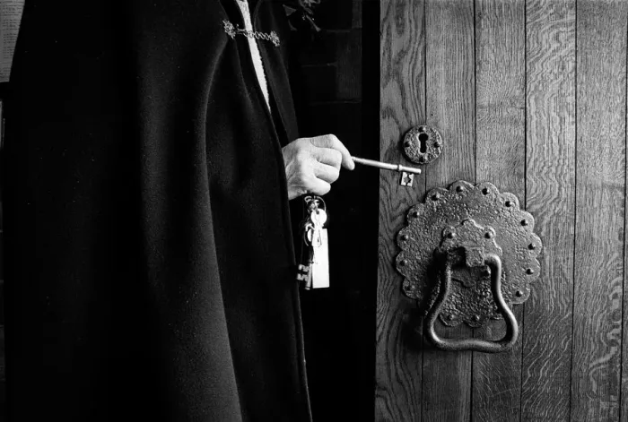 Framed Print : A priest wearing a black cloak unlocks the oak door of a chu Framed Print : A priest wearing a black cloak unlocks the oak door of a chu