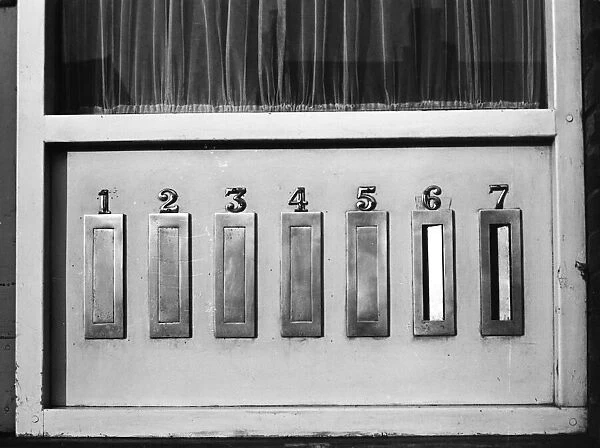 Seven identical letter boxes in a block of flats. Date: 1960s