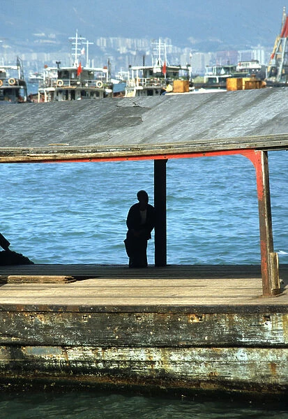 Silhouette of man sat on a bollard on a pier in Hong Kong