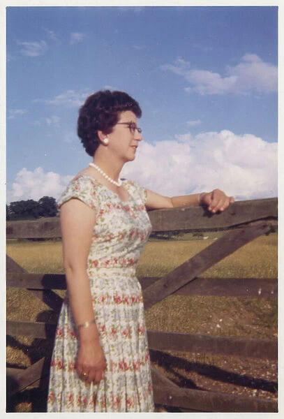 Smartly-dressed middle aged woman leaning on a gate