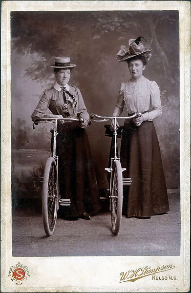 A splendid cabinet photograph of two well-dressed women standing proudly with their bicycles