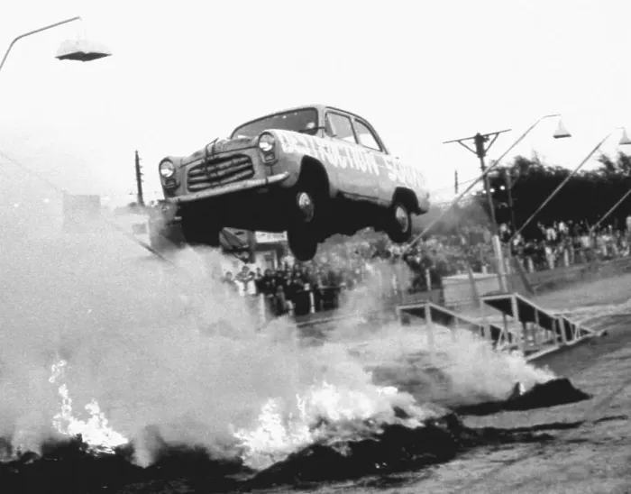 Framed Print : A stunt car flies through the air over a bonfire of tyres, watched by spectators standing in the rain. Date: 1960s Framed Print : A stunt car flies through the air over a bonfire of tyres, watched by spectators standing in the rain. Date: 1960s