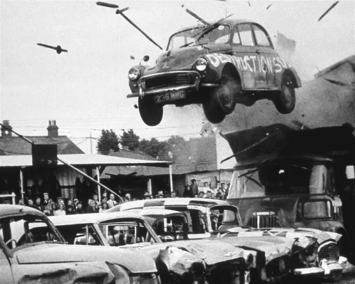 Framed Print : A stunt car flies through the air over a row of other cars, watched by spectators. Date: 1960s Framed Print : A stunt car flies through the air over a row of other cars, watched by spectators. Date: 1960s