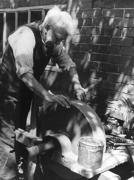 The village farrier (blacksmith) sharpening a pair of garden shears at his wheel
