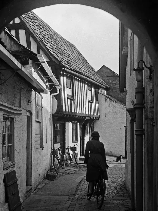 Framed Print : Woman cycling along path between houses Framed Print : Woman cycling along path between houses