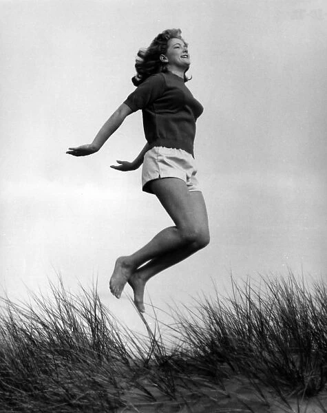 Woman in shorts and top jumping in sand dunes