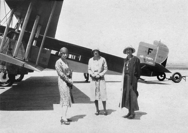 Three women in front of biplane at an airport