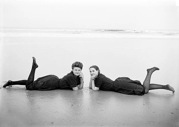 Two women in period bathing costumes lying on the beach