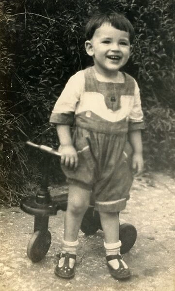 Young boy laughing. A small boy stands by his tricycle, clearly very amused by something