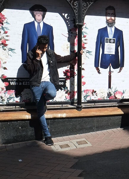 A young man in jeans sits against a fashion shop window