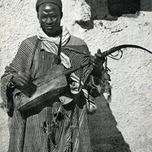 Algeria - African Gnawa Musician playing a traditional sintir, also known as the guembri, gimbri or hejhouj, a three-stringed skin-covered bass plucked lute. Date: circa 1910s