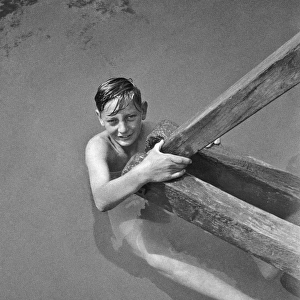 Boy swimmer holding on to wooden beam