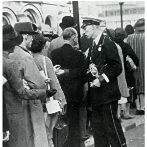 Bus conductor collecting fares from queuers, September 1939