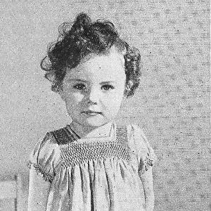 A child model wearing a smocked dress. Date: 1935