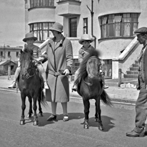 Two children riding ponies in a street