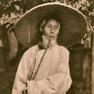 Elderly Chinese man in hat smoking a long pipe