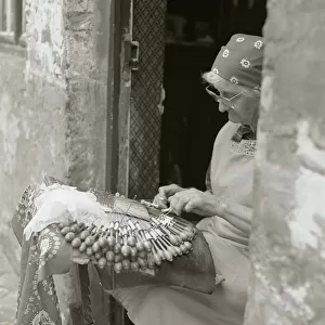 Elderly woman making lace in an open doorway