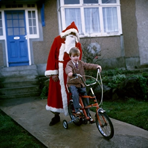 Father Christmas stands behind boy on bike