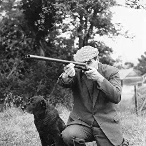 Gamekeeper taking aim, his dog at his side