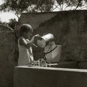 Girl pouring water from a tin into a bucket